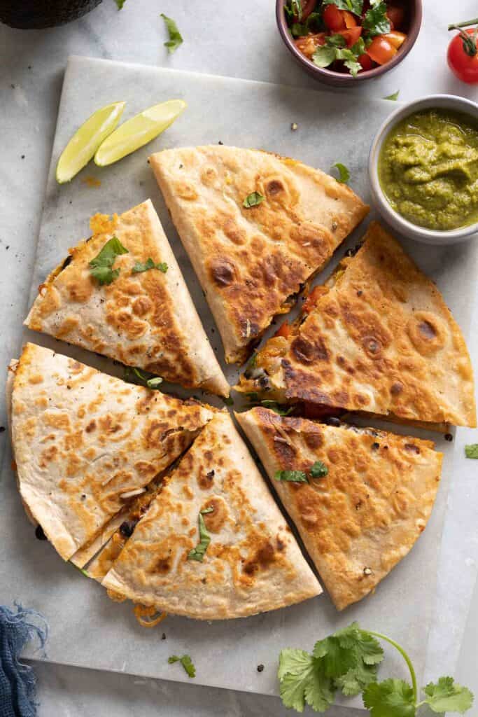 Two Sweet Potato & Black Bean Quesadillas arranged in circle and cut into 6 wedges on serving board with fresh cilantro and bowls of salsa  on the side.