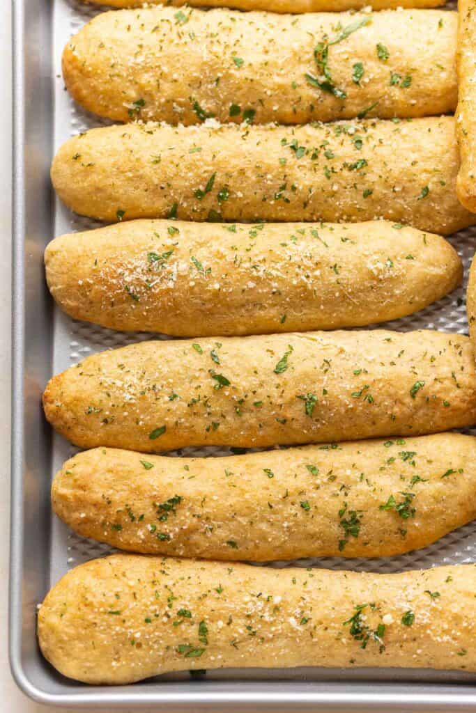 Gluten free breadsticks on a cookie sheet topped with grated parmesan and parsley.