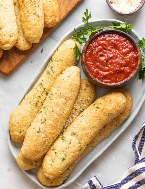 Gluten free breadsticks on a platter with a bowl of marinara dipping sauce.