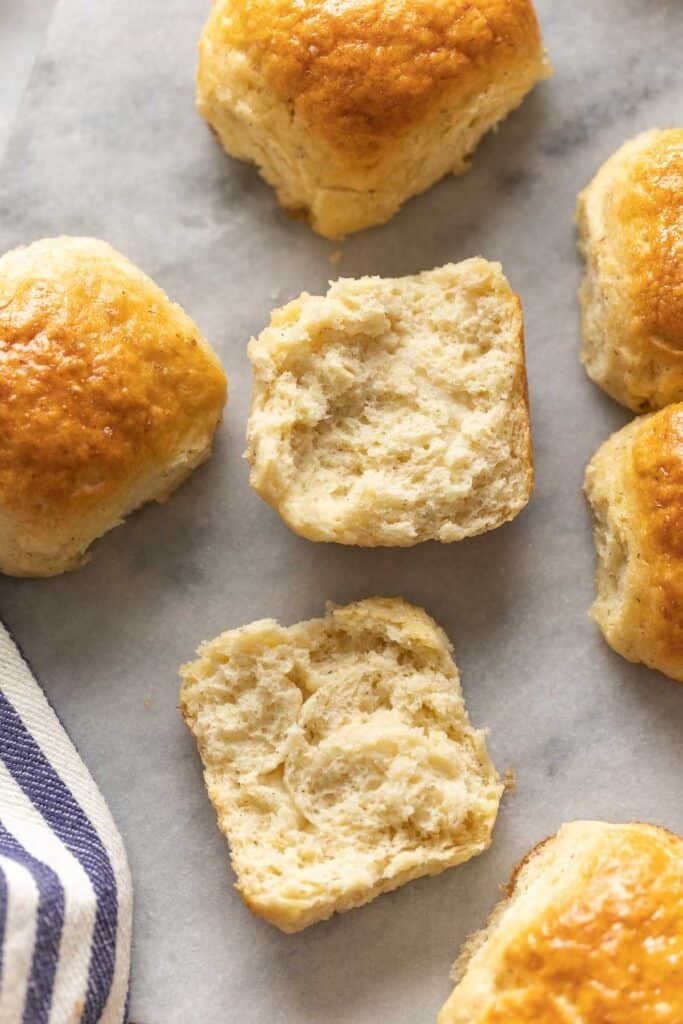 Gluten free dinner rolls on a marble surface - one dinner roll opened up to show the soft inside.