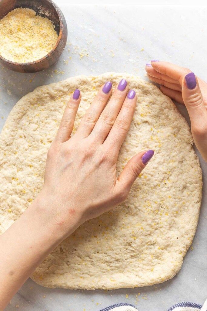 Homemade gluten free pizza dough getting gently stretched and pressed into a large circle.