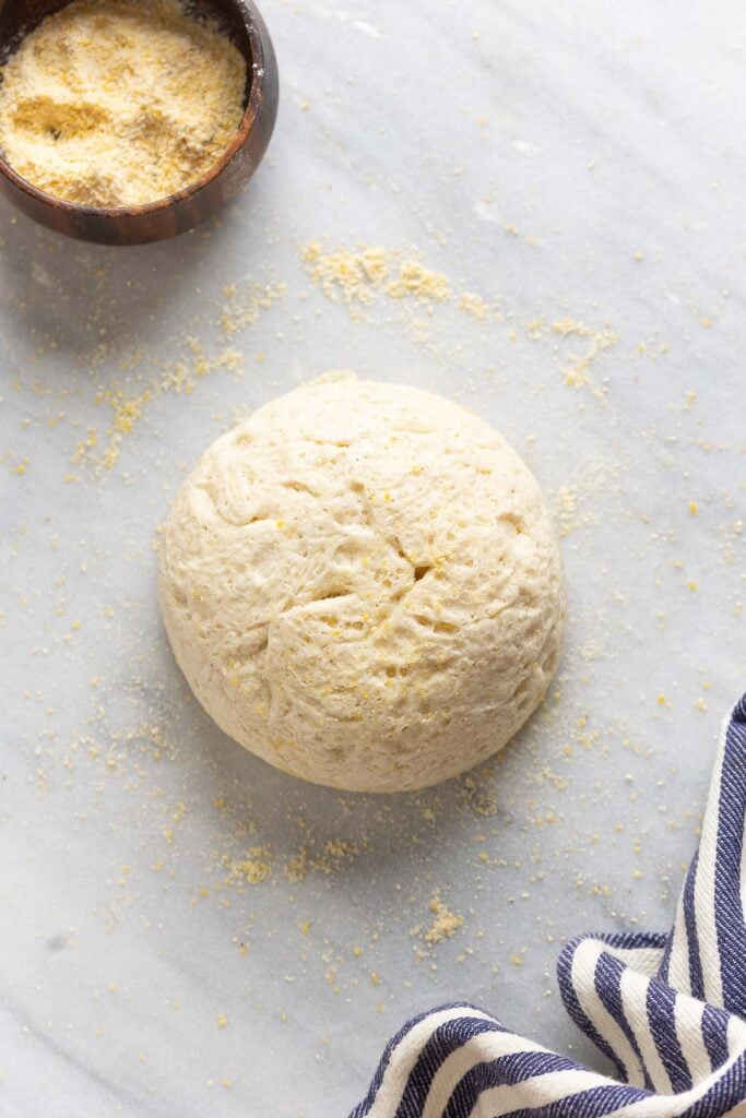 Homemade gluten free pizza dough ball on surface lightly dusted with cornmeal.