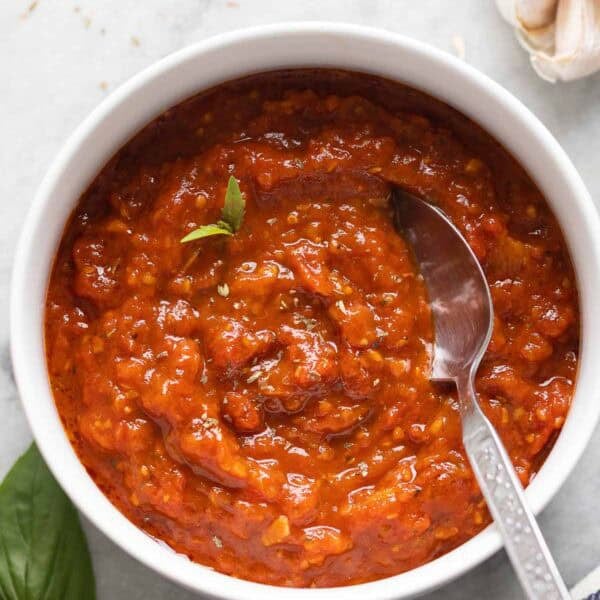 Homemade Pizza Sauce in a bowl with a couple fresh basil leaves and a spoon. Garlic head and fresh basil spring on the side.