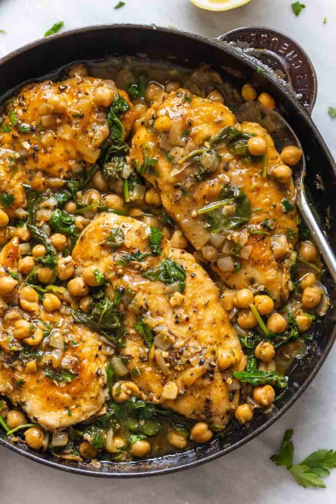 A cast iron skillet full of of Pan Seared Chicken & Chickpeas in a Lemon-Anchovy Sauce with fresh parsley sprinkled around the pan.