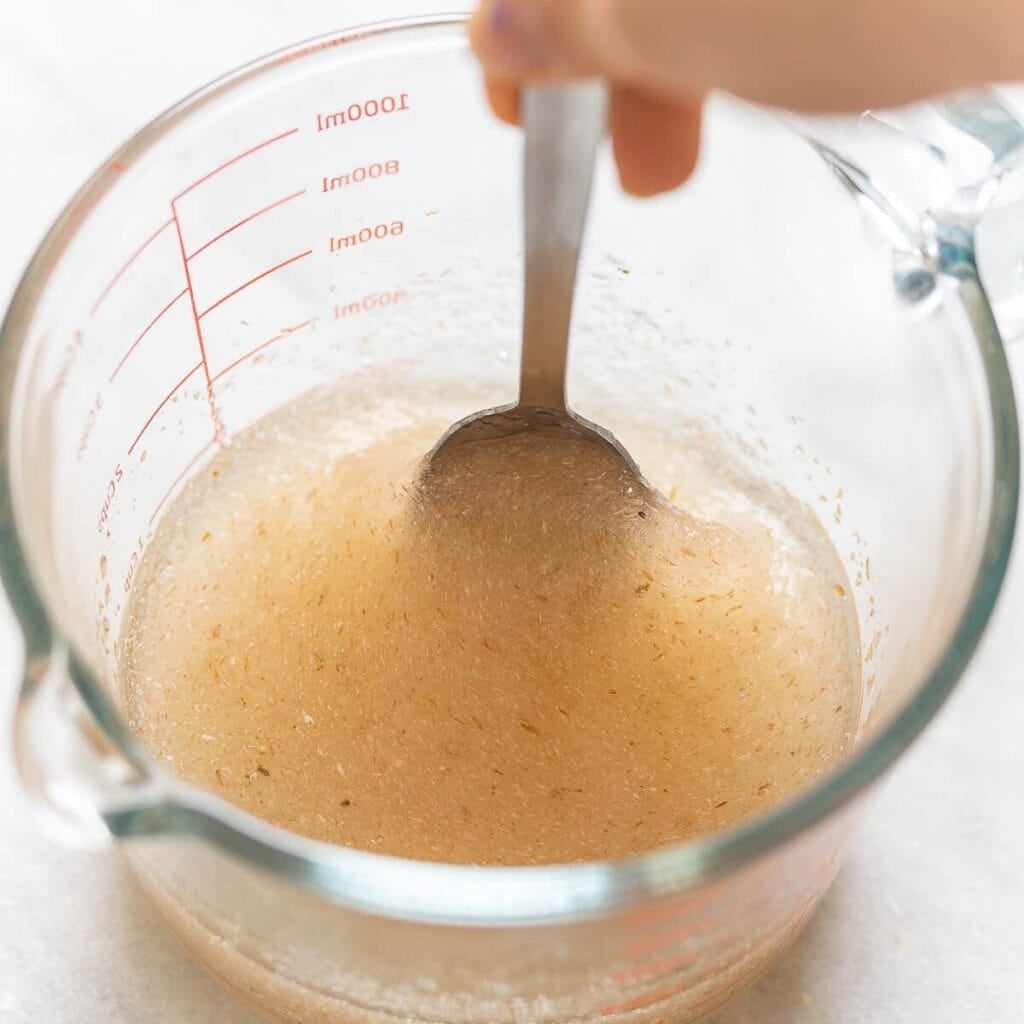 A hand mixing whole psyllium husk and water together in a measuring jug.