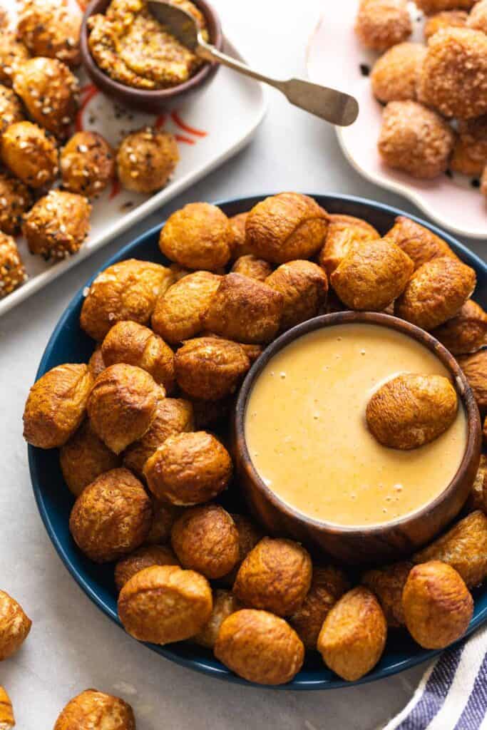 Gluten Free Pretzel Bites on a plate with a bowl of cheese sauce and aa pretzel bite in the cheese sauce.