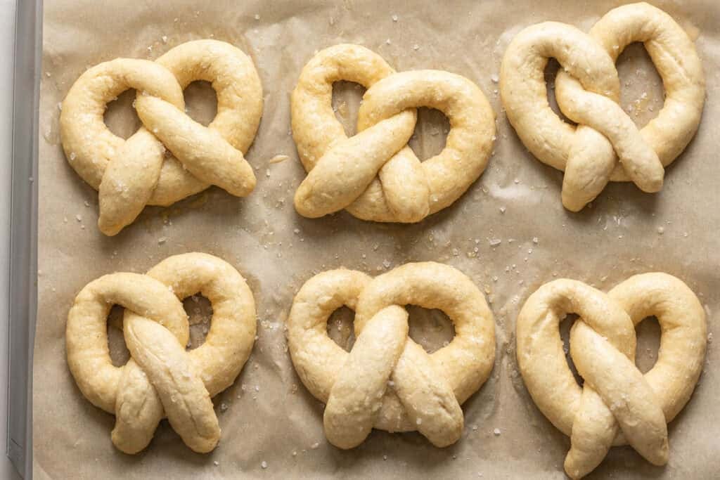 Six gluten free soft pretzels dough on a baking sheet.