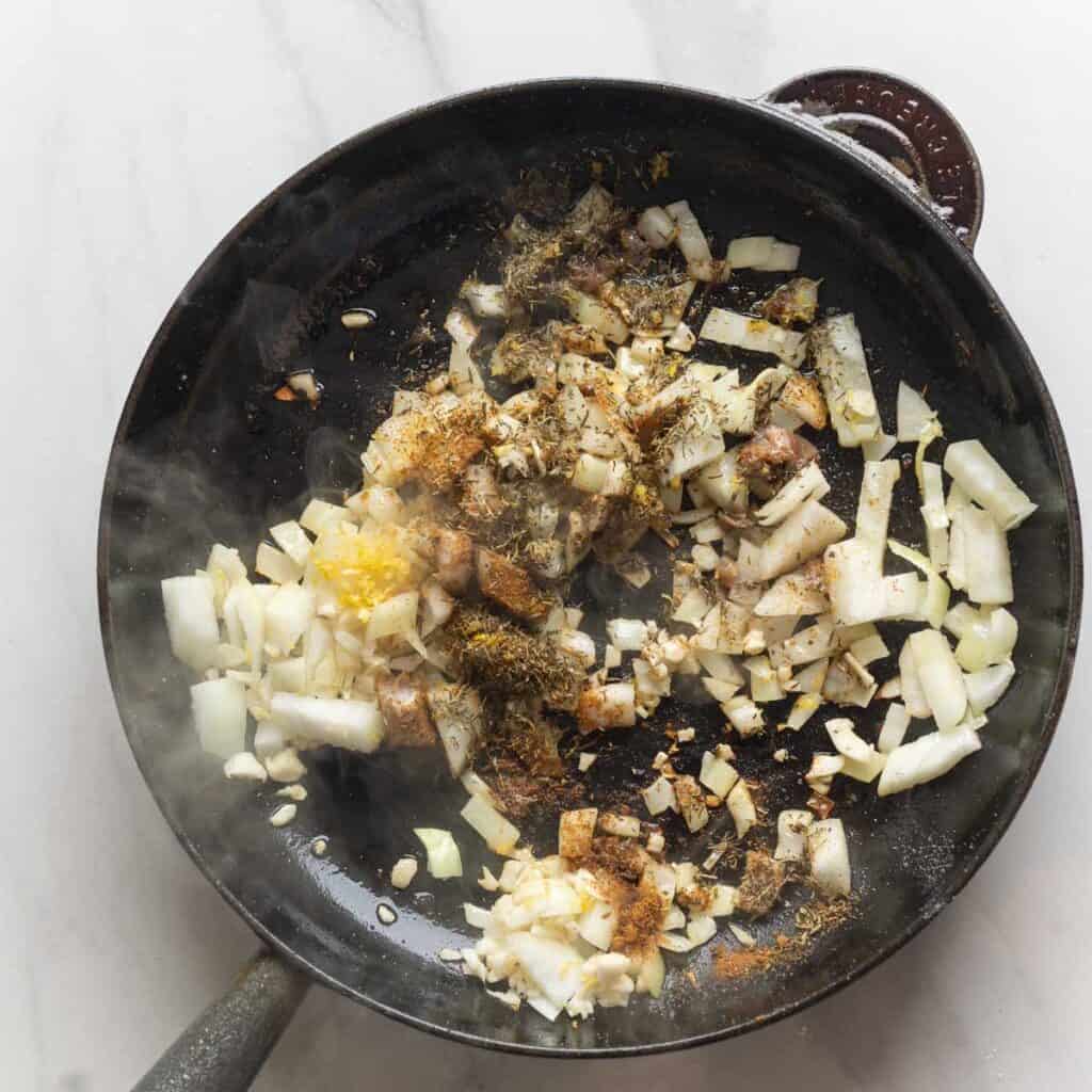 Chopped onions, garlic, lemon zest, chopped anchovies, dried thyme and  ground cumin in a cast iron skillet.