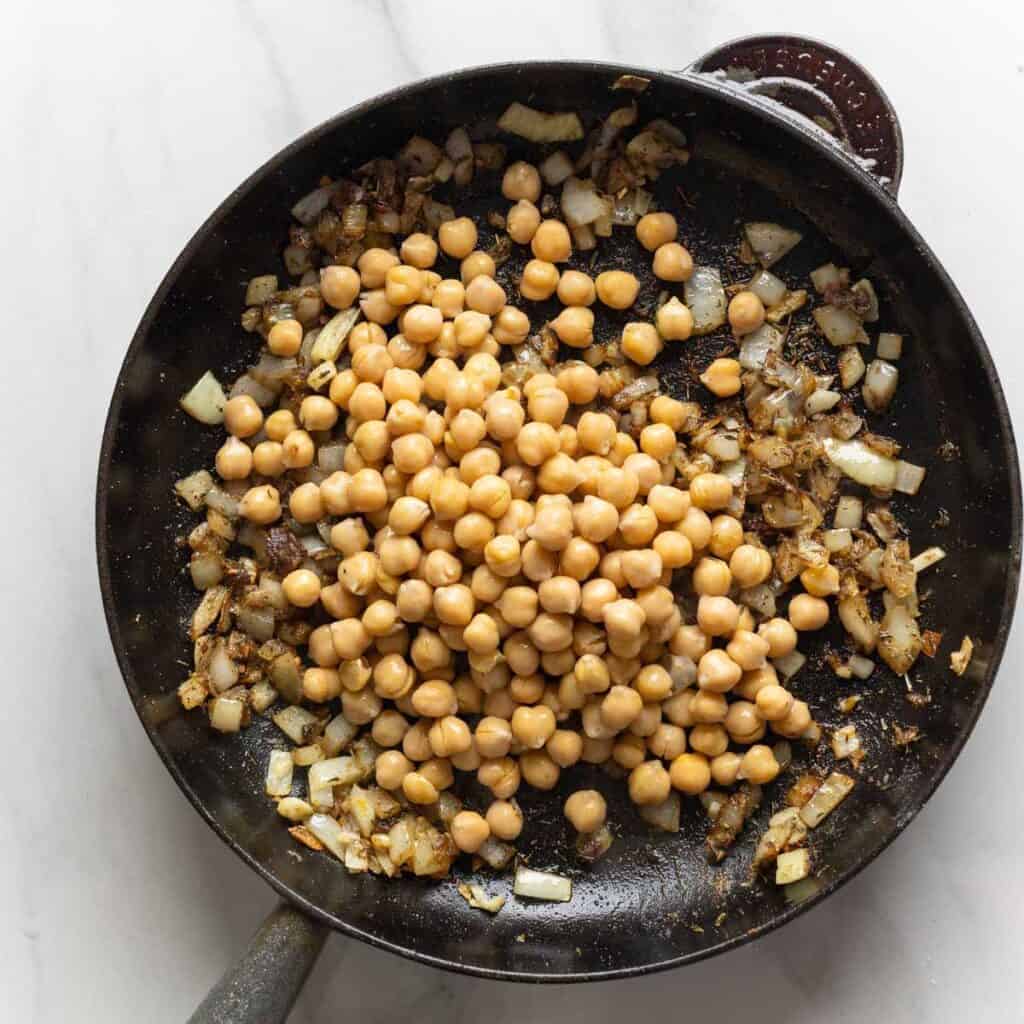 Cooked chickpeas on top of sautéed aromatics in a cast iron skillet.