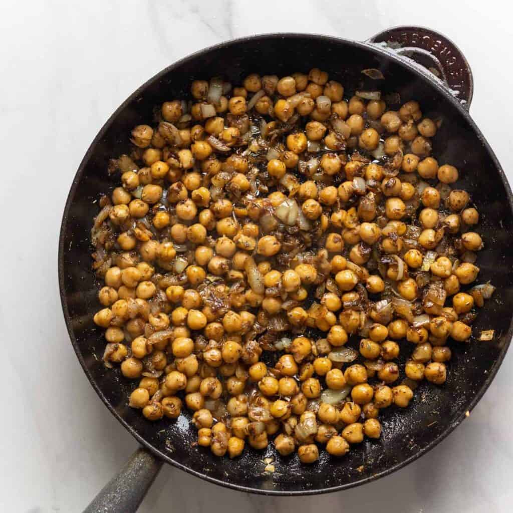 Sautéed chickpeas and aromatics inside a cast iron skillet.