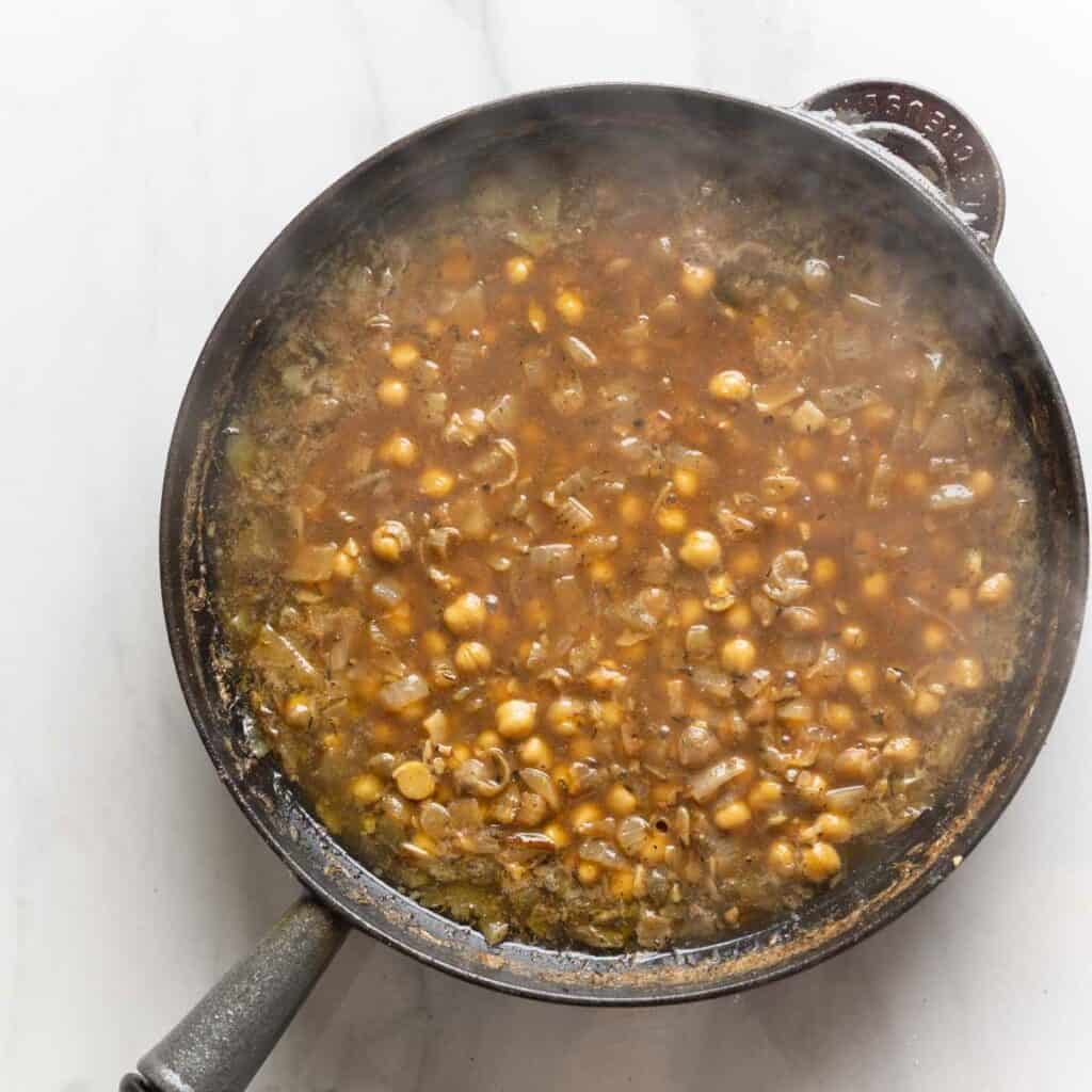 A cast iron skillet full of a lemon-anchovy sauce with chickpeas that has been simmered to create a thicker sauce.