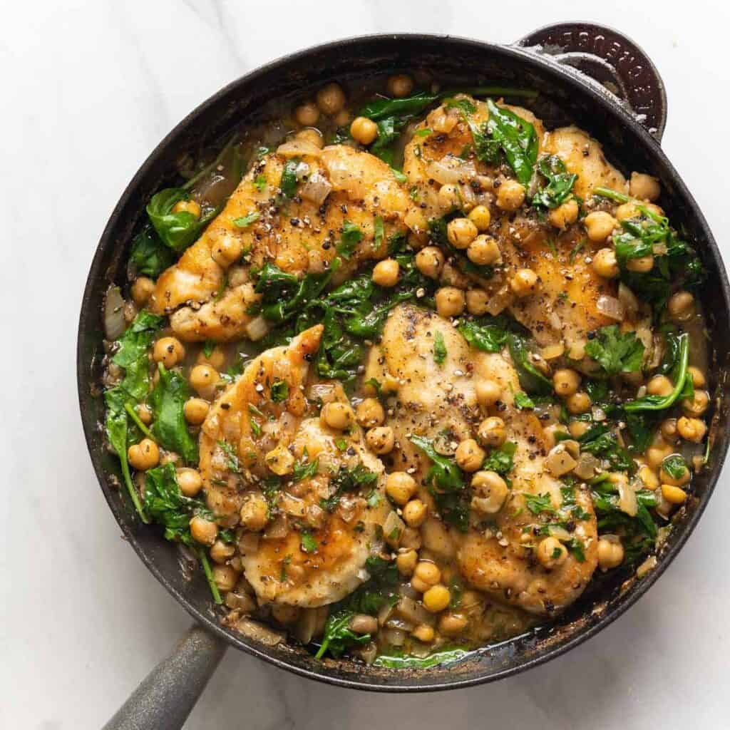 Pan seared chicken mixed into a skillet full of lemon-anchovy simmer chickpeas and wilted spinach.
