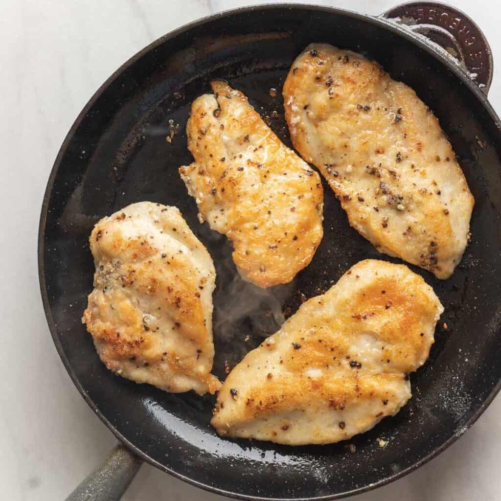 Four chicken breasts coated in salt, pepper and gluten free flour seared in a cast iron skillet on both sides.