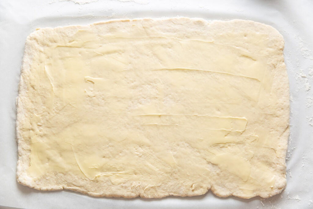Gluten free cinnamon roll dough rolled out in a big rectangle with softened butter spread over the surface.