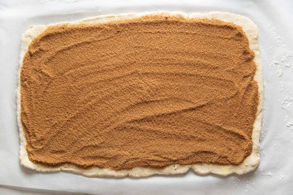 Gluten free cinnamon roll dough rolled out in a big rectangle then covered with a butter, cinnamon-sugar mixture.