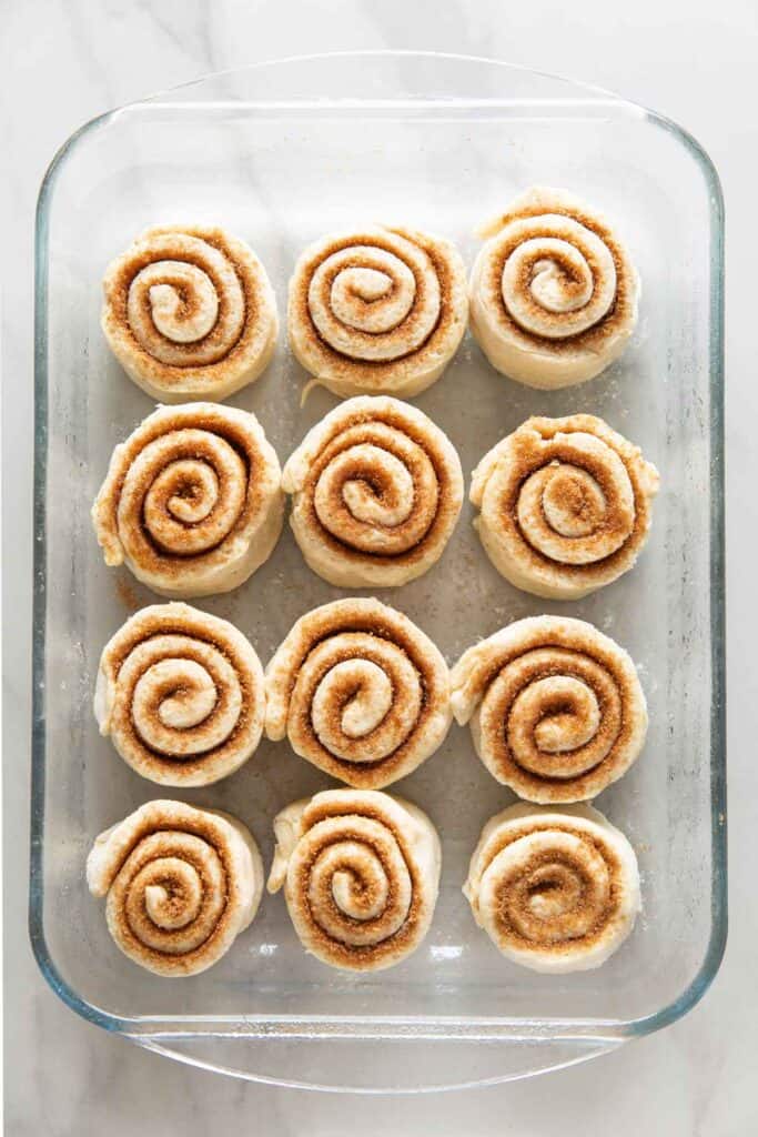 A glass baking dished, lightly greased and filled with 12 unbaked, un-rise gluten free cinnamon rolls.
