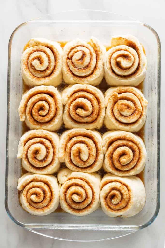 A glass baking dished, lightly greased and filled with 12 unbaked gluten free cinnamon rolls after they've had time to proof & puff up.