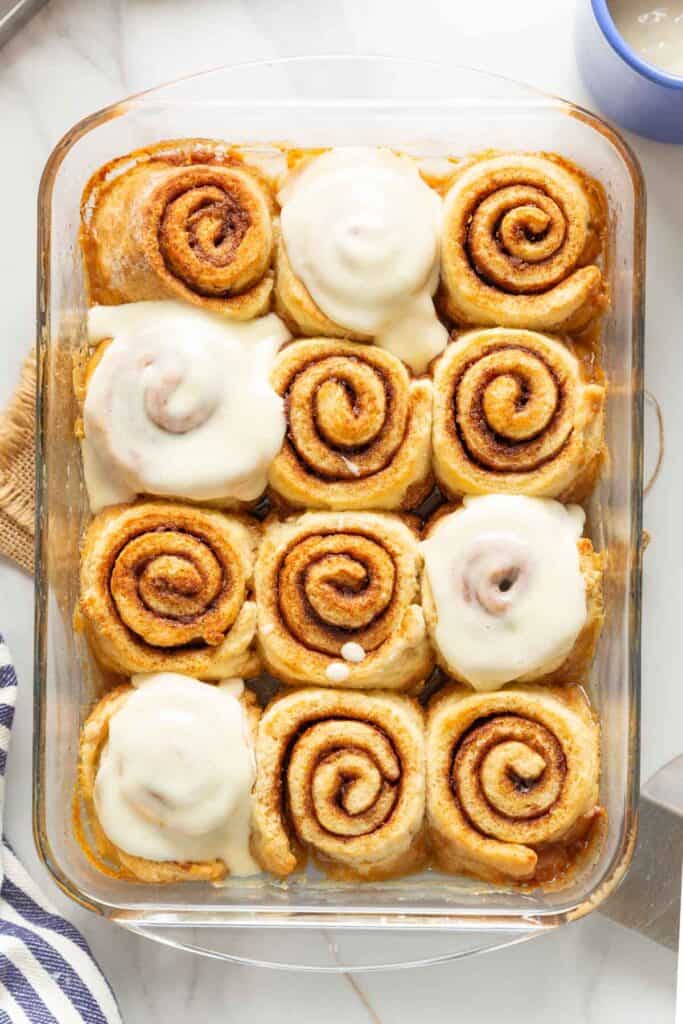 A glass baking dish filled with gluten-free cinnamon rolls, some with a cream cheese frosting on top.