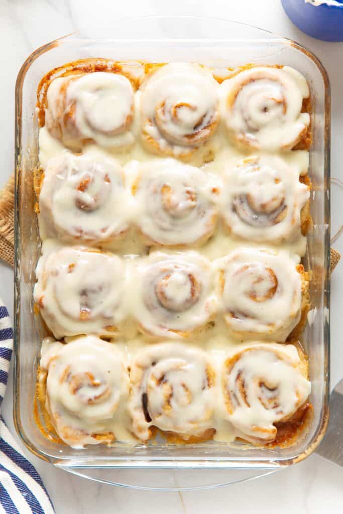 A glass baking dish full of 12 homemade gluten free cinnamon rolls covered in a cream cheese frosting.