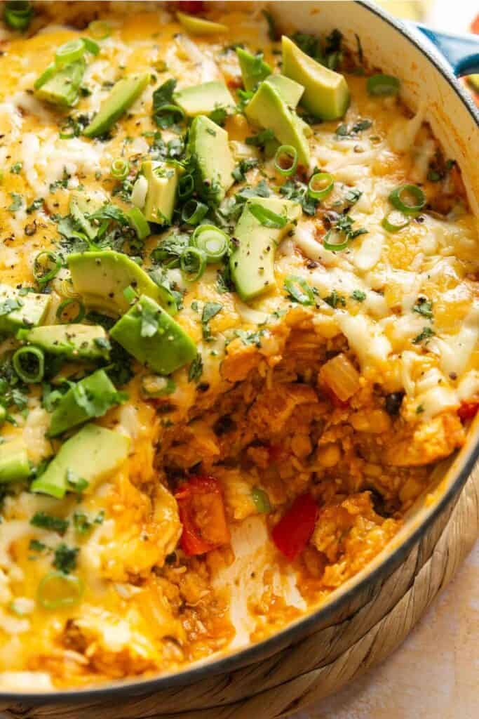 A cheesy enchilada rice casserole missing from the serving dish to show casserole ingredients: rice, beans, corn and red pepper pepper.