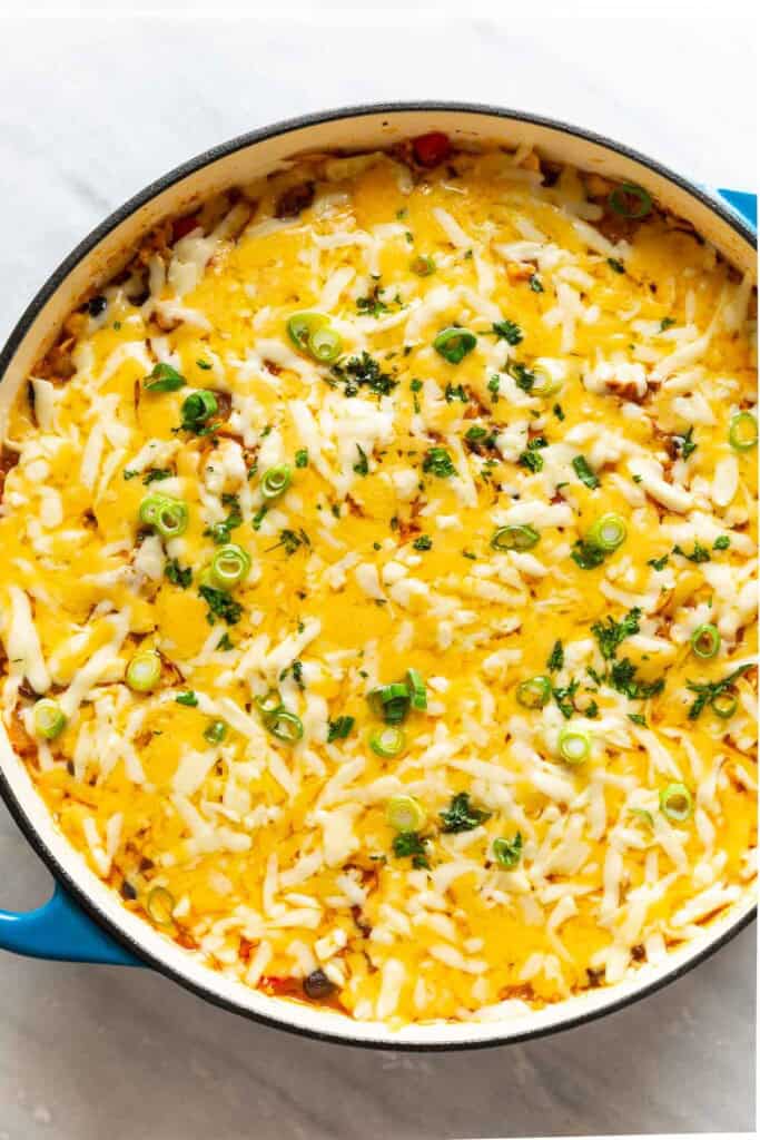 A casserole dish full of cheesy chicken enchilada rice with green onions and fresh cilantro on top. 