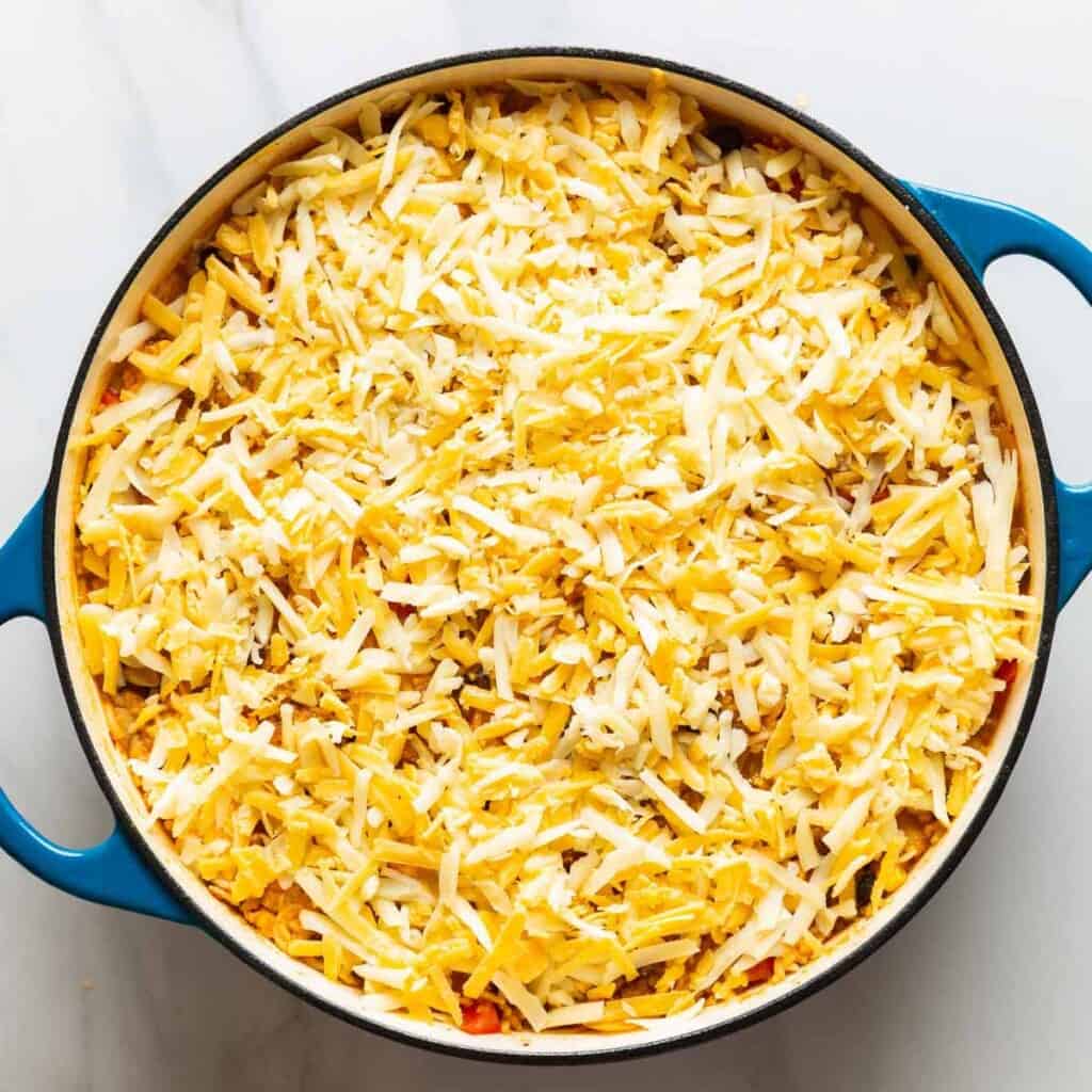 A casserole dish full of Chicken & Enchilada Rice with grated cheese on top before it's been melted.