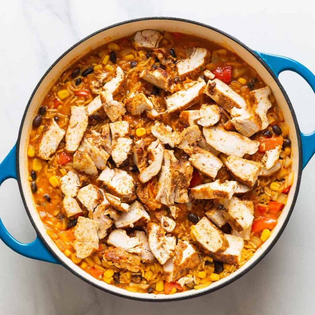 A casserole dish full of One Pot Cheesy Chicken & Enchilada Rice shown after the cooked and sliced chicken has been added back to the rice mixture.
