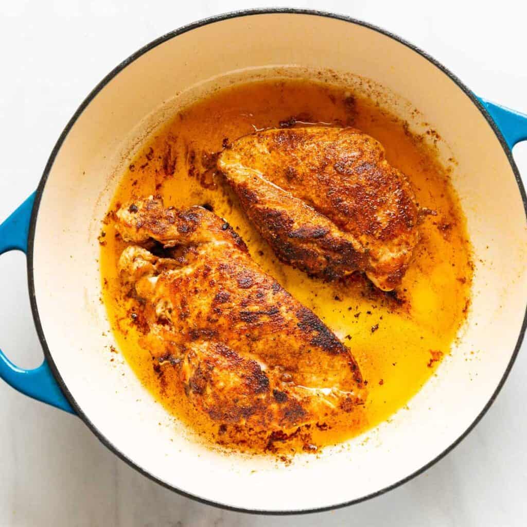 Two seasoned chicken breasts searing in a large pan.