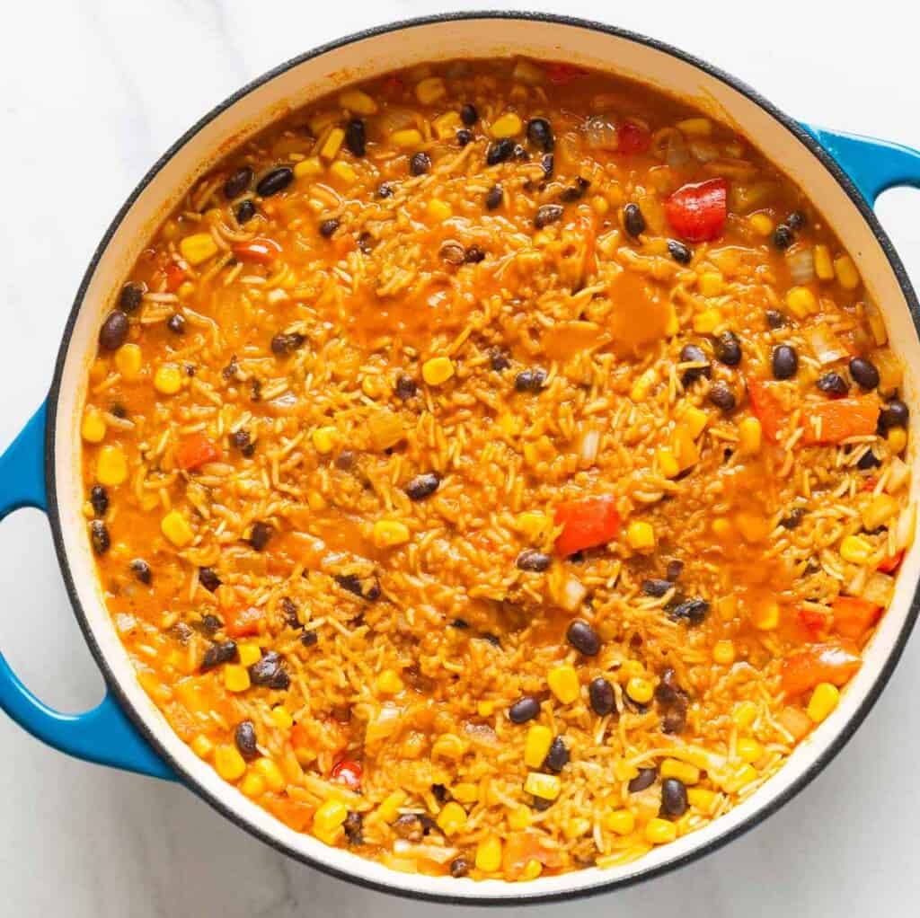 A casserole dish full of One Pot Cheesy Chicken & Enchilada Rice shown after it's almost done cooking with some liquid left.
