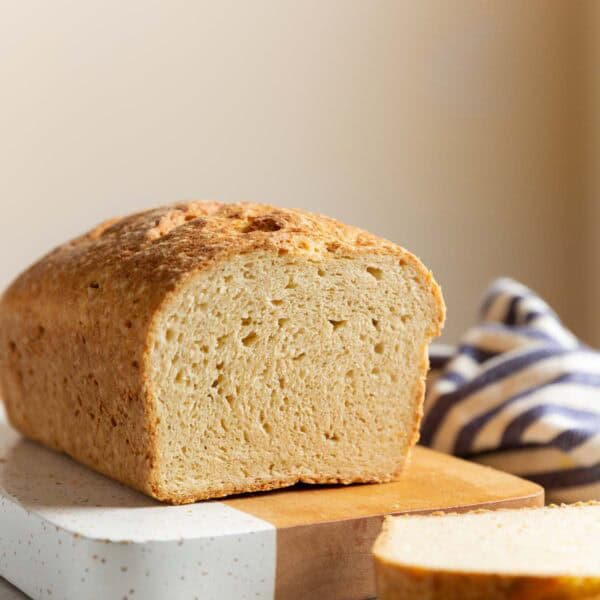 A loaf of Gluten Free Sandwich Bread on a cutting board with a couple of slices cut off the end to expose the inside texture.