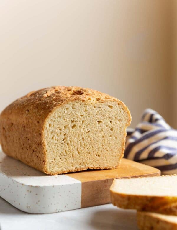 A loaf of Gluten Free Sandwich Bread on a cutting board with a couple of slices cut off the end to expose the inside texture.