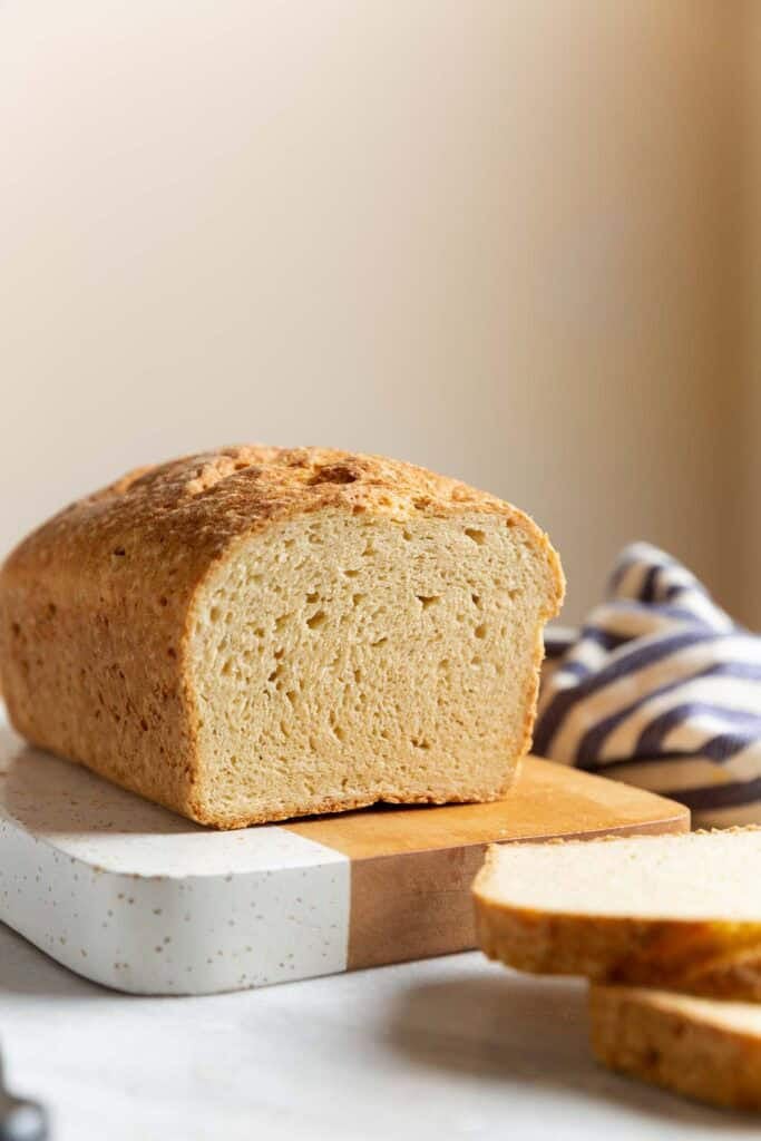 A loaf of Gluten Free Sandwich Bread on a cutting board with a couple of slices cut off the end to expose the inside texture.