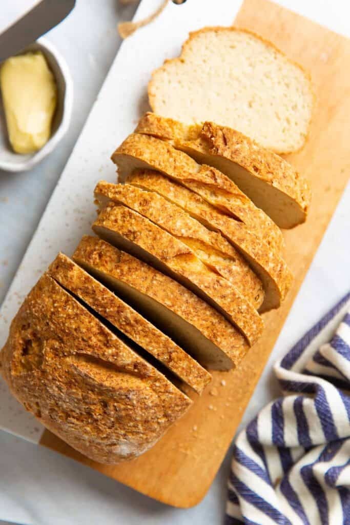 A Gluten Free Sandwich Bread loaf on a cutting board cut into slices and a small bowl of butter on the side.