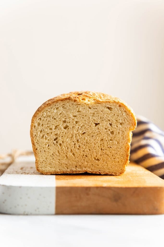 A loaf of Gluten Free Sandwich Bread on a cutting board with a slice cut off the end.