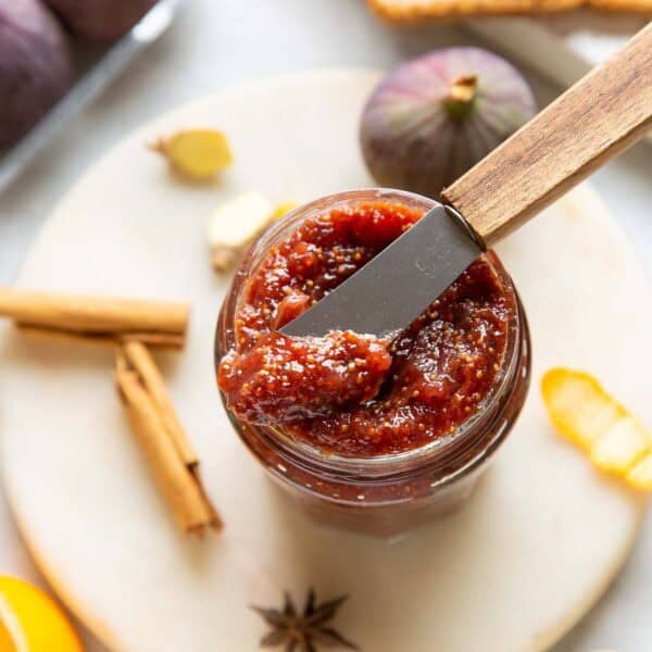 A small butter knife placed over a jar of homemade fig jam with the fresh ingredients surrounding the jar.