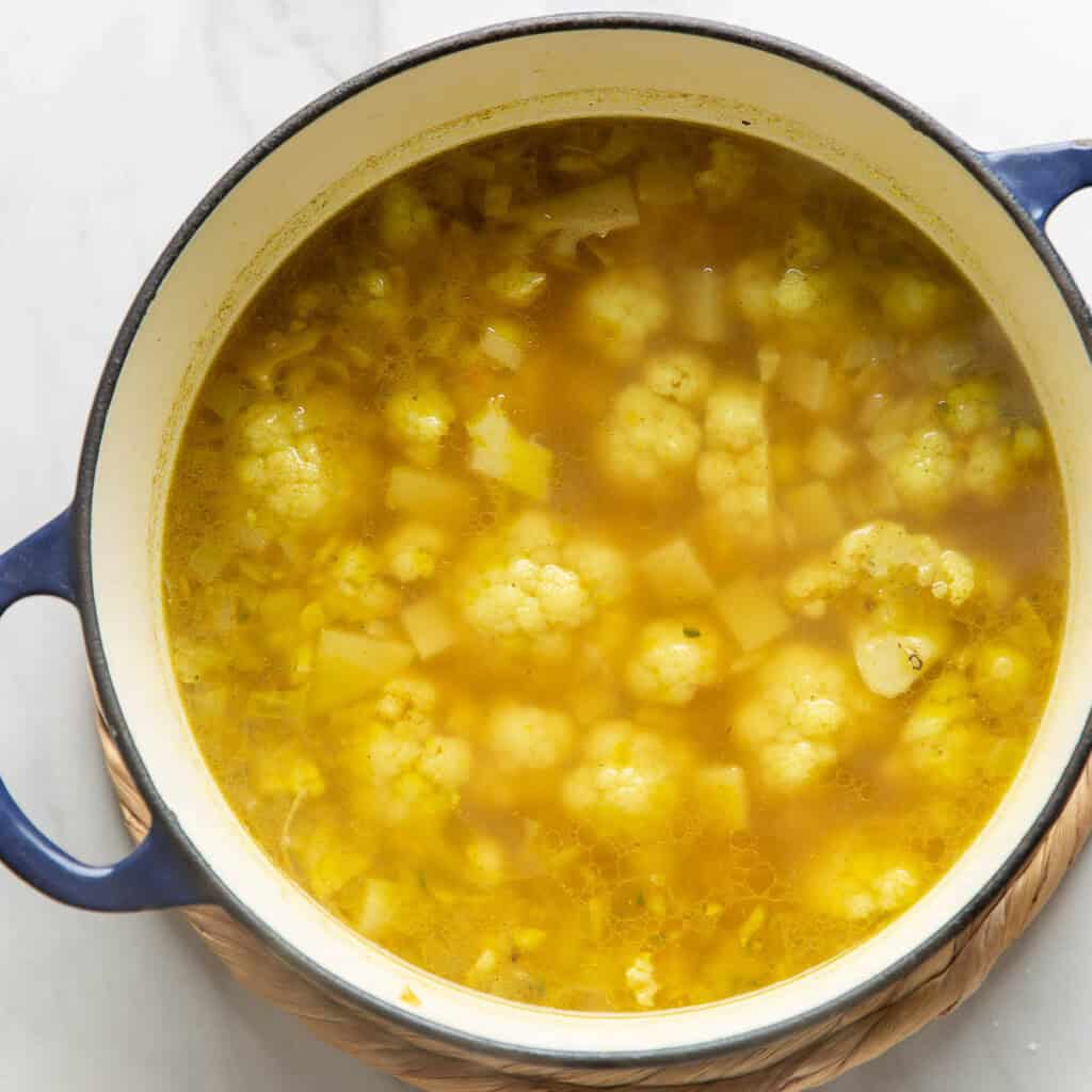 A large dutch oven pot full of diced potato and cauliflower florets mixed into a spiced onion mixture after simmering until the veggies are soft.