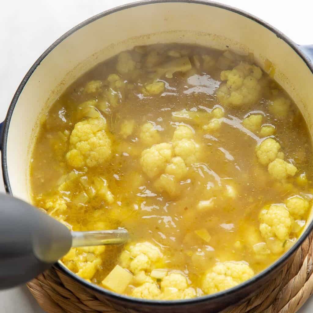 An immersion blender blending up a soup made with curried potatoes and cauliflower.