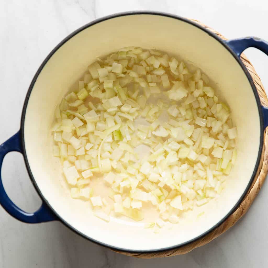 A large dutch oven pot with diced onion and oil.