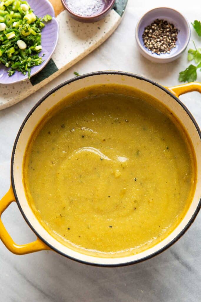 A dutch oven full of a pureed aloo gobi soup (curried potato and cauliflower soup) with garnishes on the side.