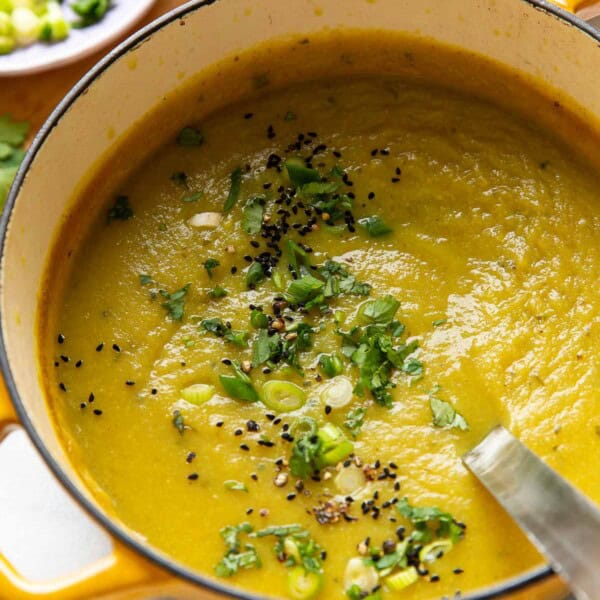 A dutch oven full of a pureed aloo gobi soup (curried potato and cauliflower soup) topped with sliced spring onions, chopped cilantro, black pepper and nigella seeds.