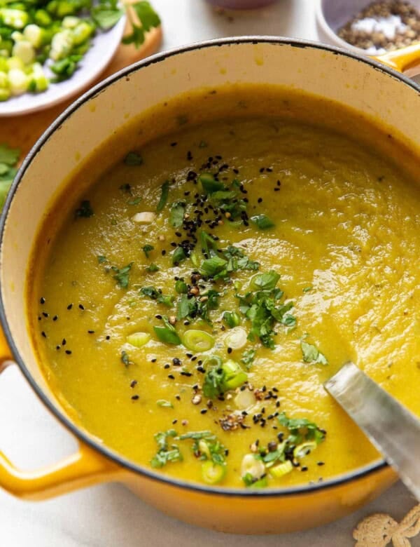 A dutch oven full of a pureed aloo gobi soup (curried potato and cauliflower soup) topped with sliced spring onions, chopped cilantro, black pepper and nigella seeds.