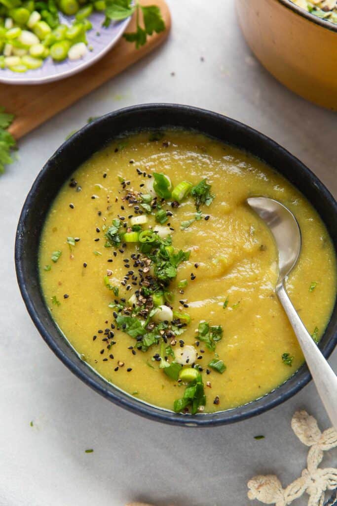 A bowl of aloo gobi soup topped spring onions, cilantro, black pepper and nigella seeds.