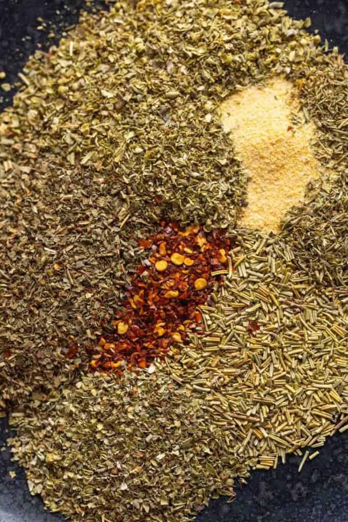 Unmixed Homemade Italian Seasoning spices on a plate: oregano, basil, thyme, rosemary, marjoram, red chili flakes and garlic powder