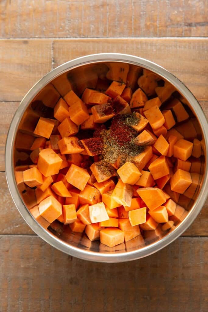 Diced sweet potato in a mixing bowl with dried spices.