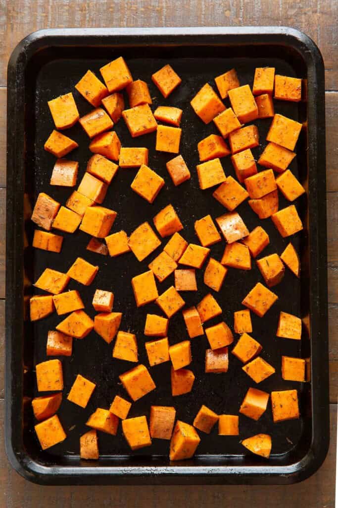 Raw, diced sweet potato coated in an oil and spice blend spread out on a backing sheet.