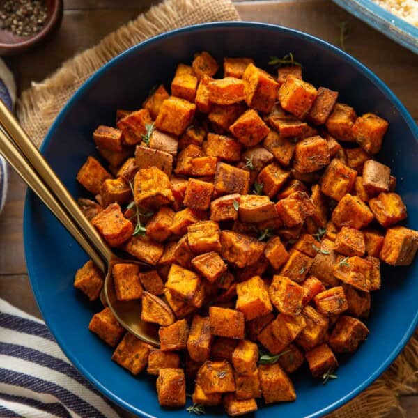 A serving dish with roasted sweet potatoes with serving spoons in the bowl and cooked quinoa on the side.