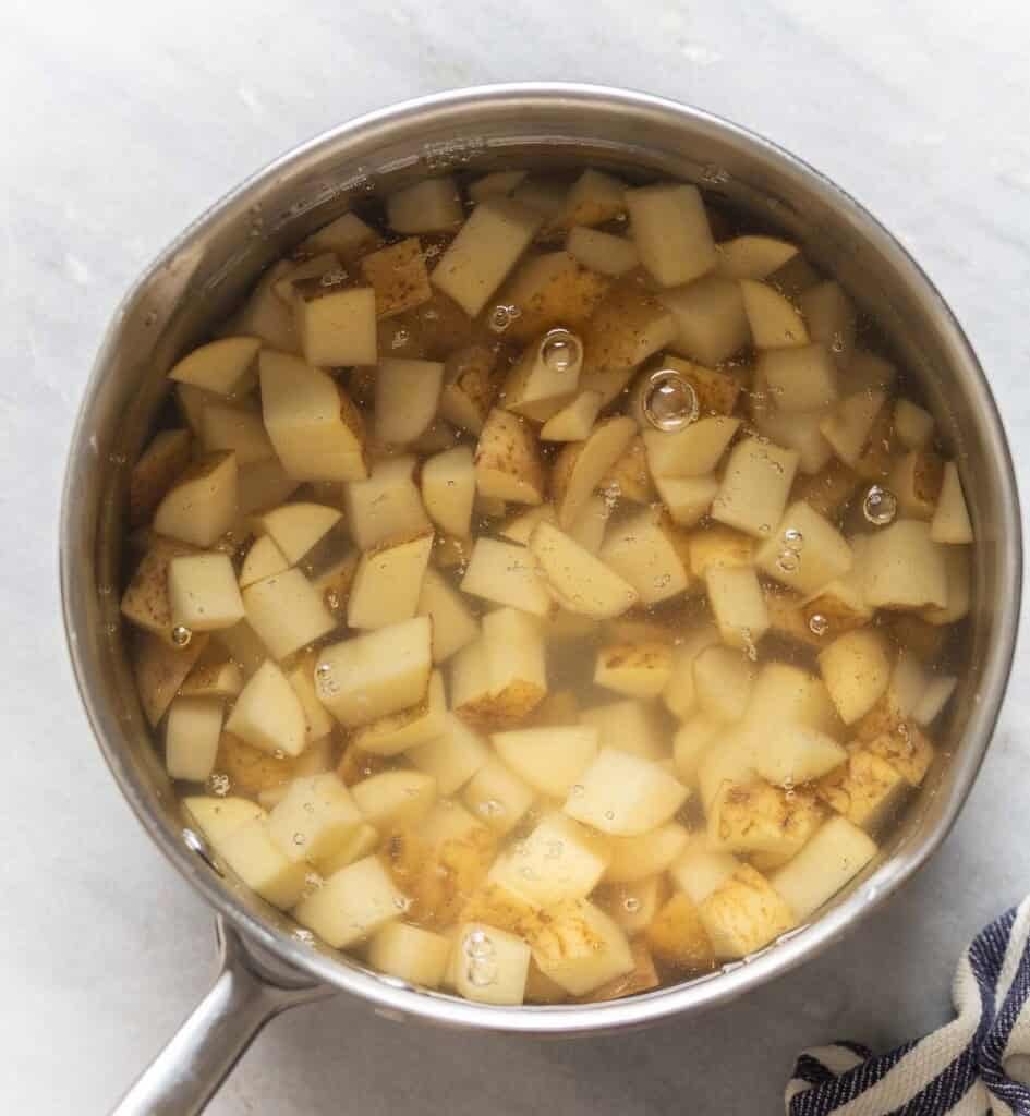 A small pot full of water covering starchy potatoes cut into 1/2-inch pieces.