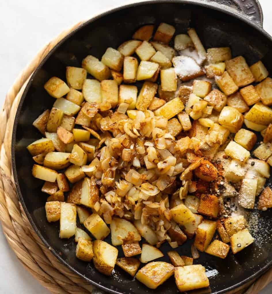Potatoes fried in a cast iron skillet until golden and crisp with sautéd onion and spices added to the potatoes.