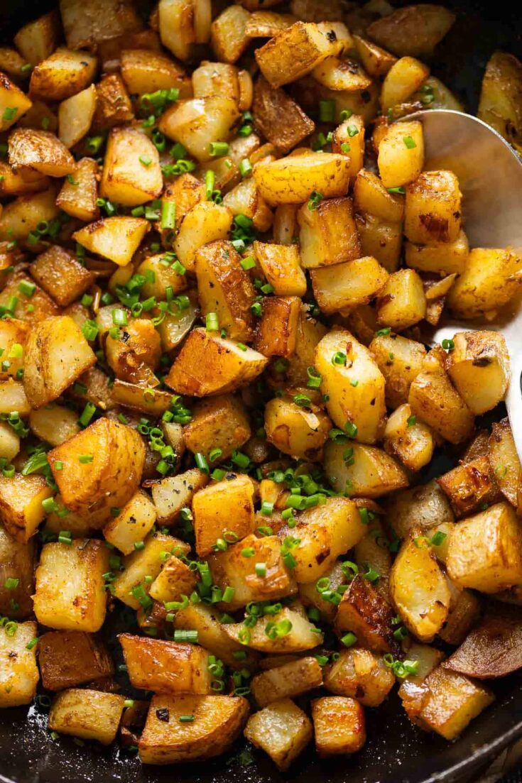Skillet Breakfast Potatoes topped with fresh chopped chives in a cast iron pan.