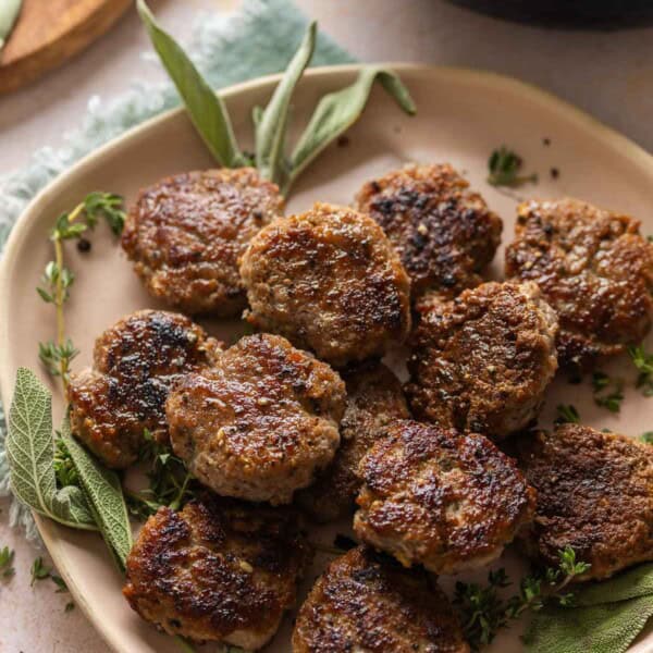 Turkey Maple Breakfast Sausage Patties on a serving plate with fresh sage and thyme.